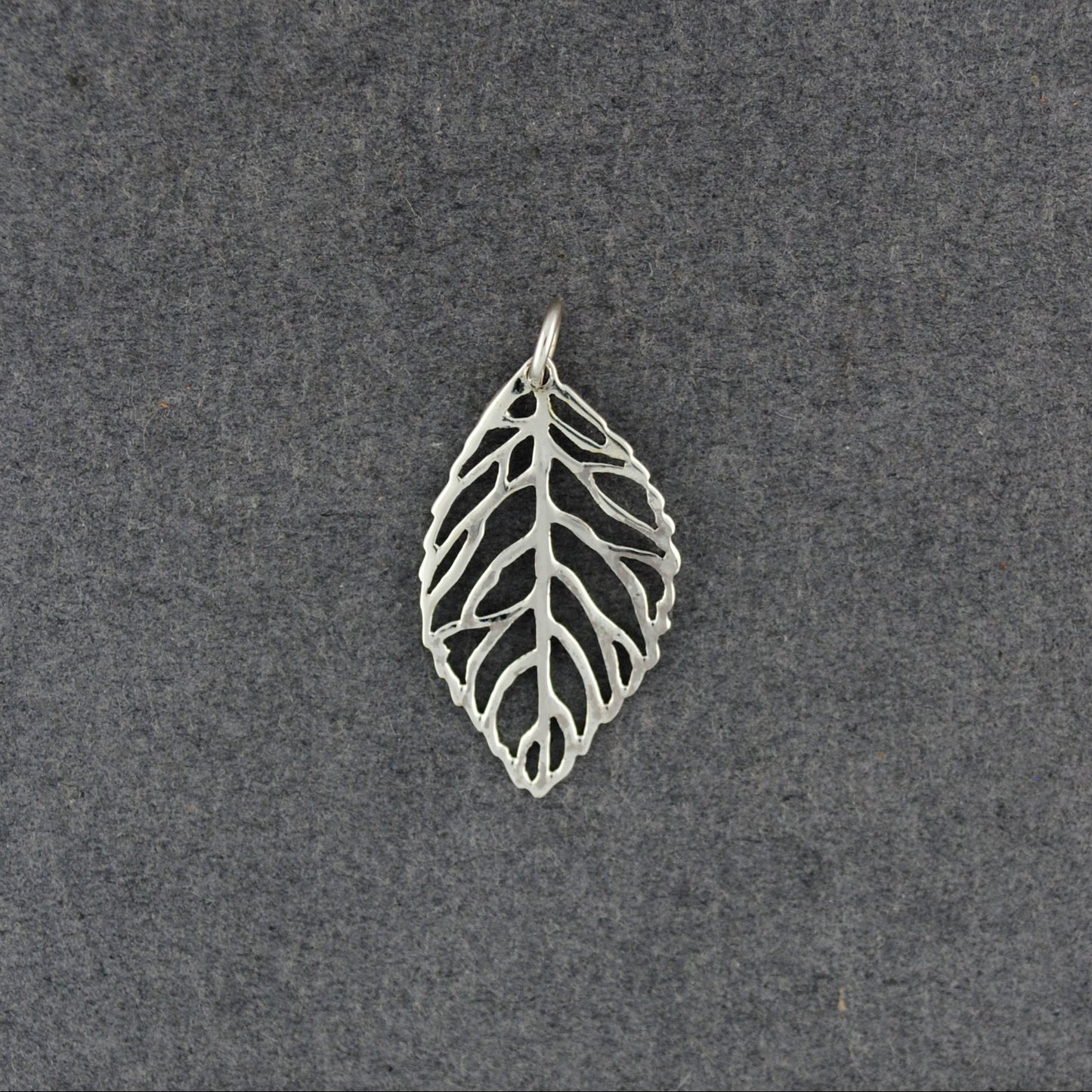 A silver leaf-shaped pendant with an openwork, vein-like design, displayed on a textured dark gray background.