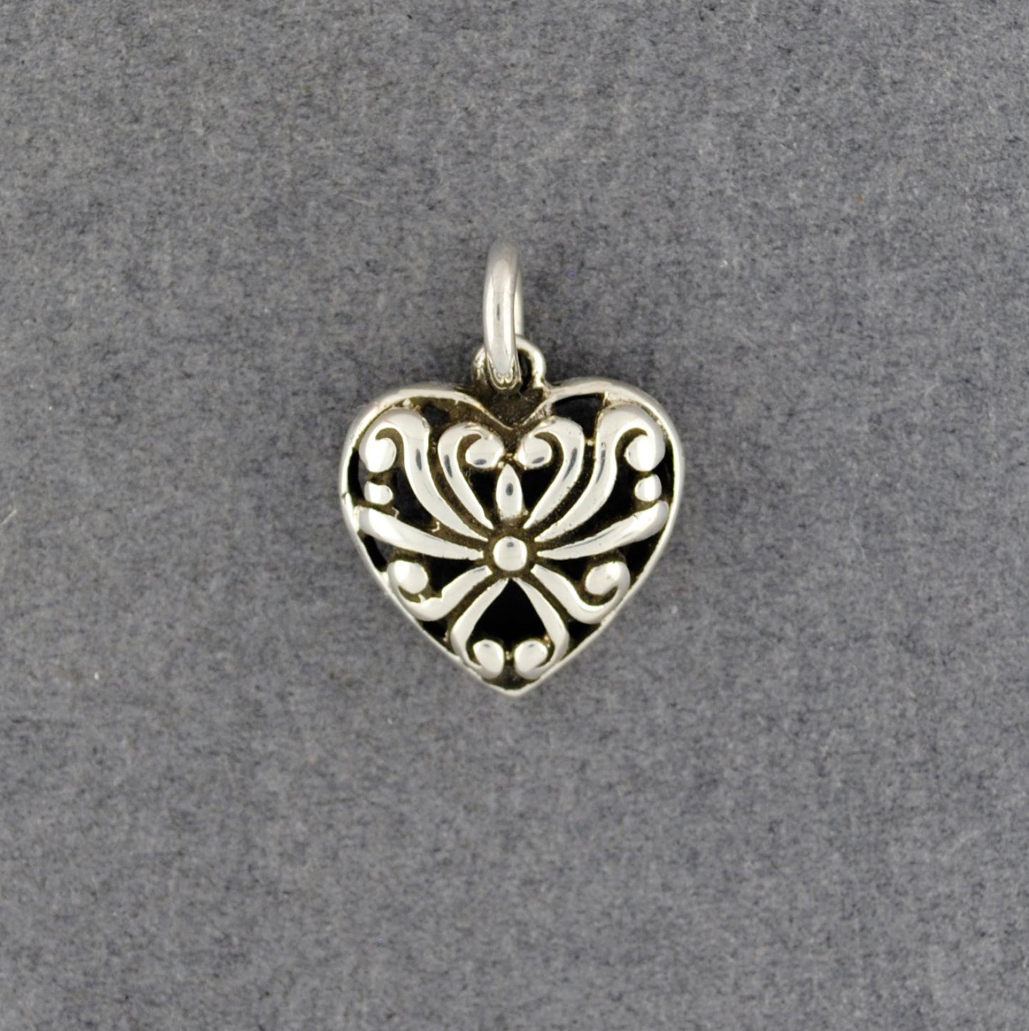 Silver heart-shaped pendant with intricate design on a gray background