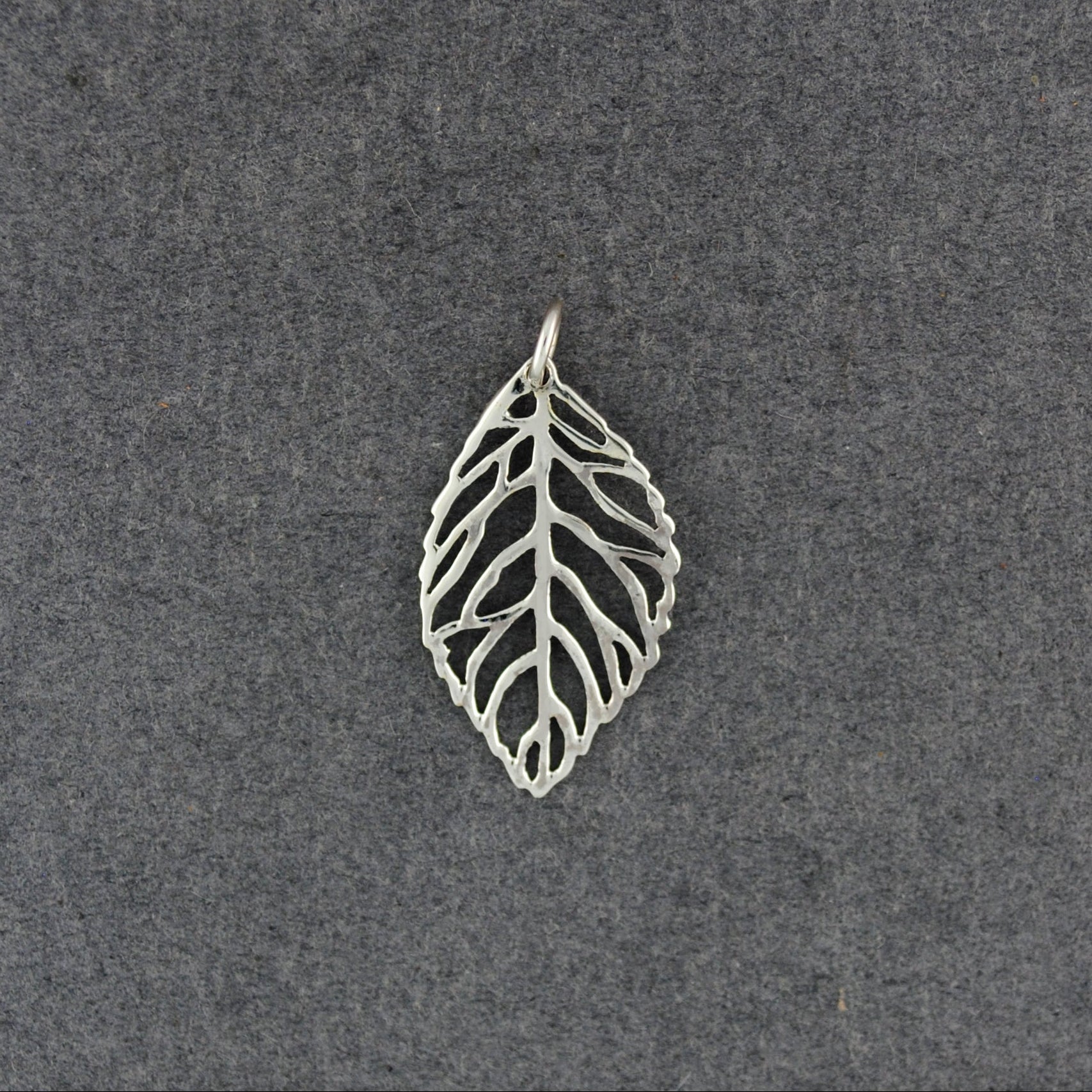 A silver leaf-shaped pendant with an openwork, vein-like design, displayed on a textured dark gray background.